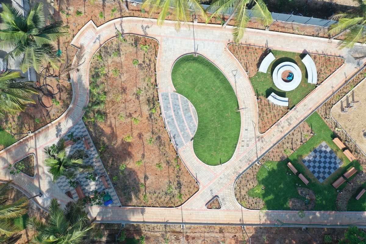 Top-down view of curved paved pathways around a green lawn and plaza